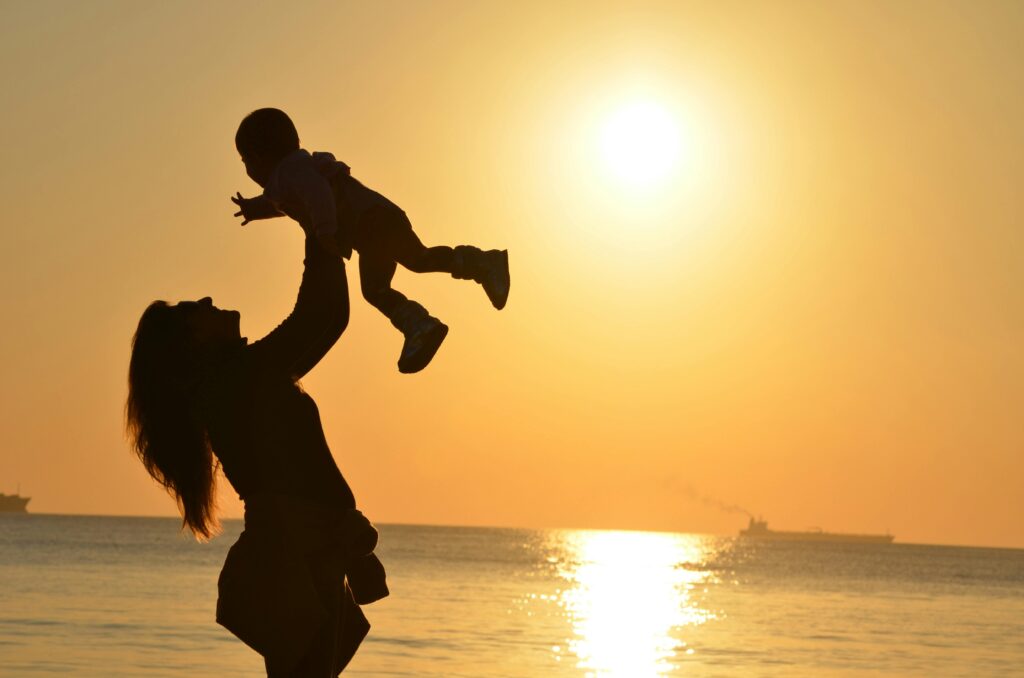 Madre levantando a su hijo frente al mar al atardecer