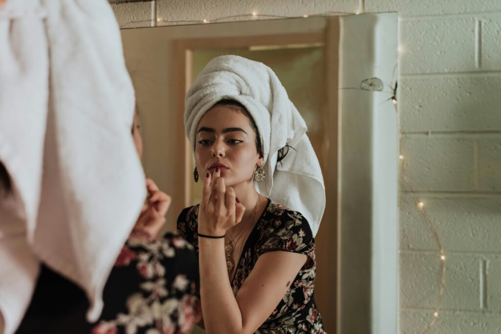 Mujer joven aplicando producto facial frente al espejo
